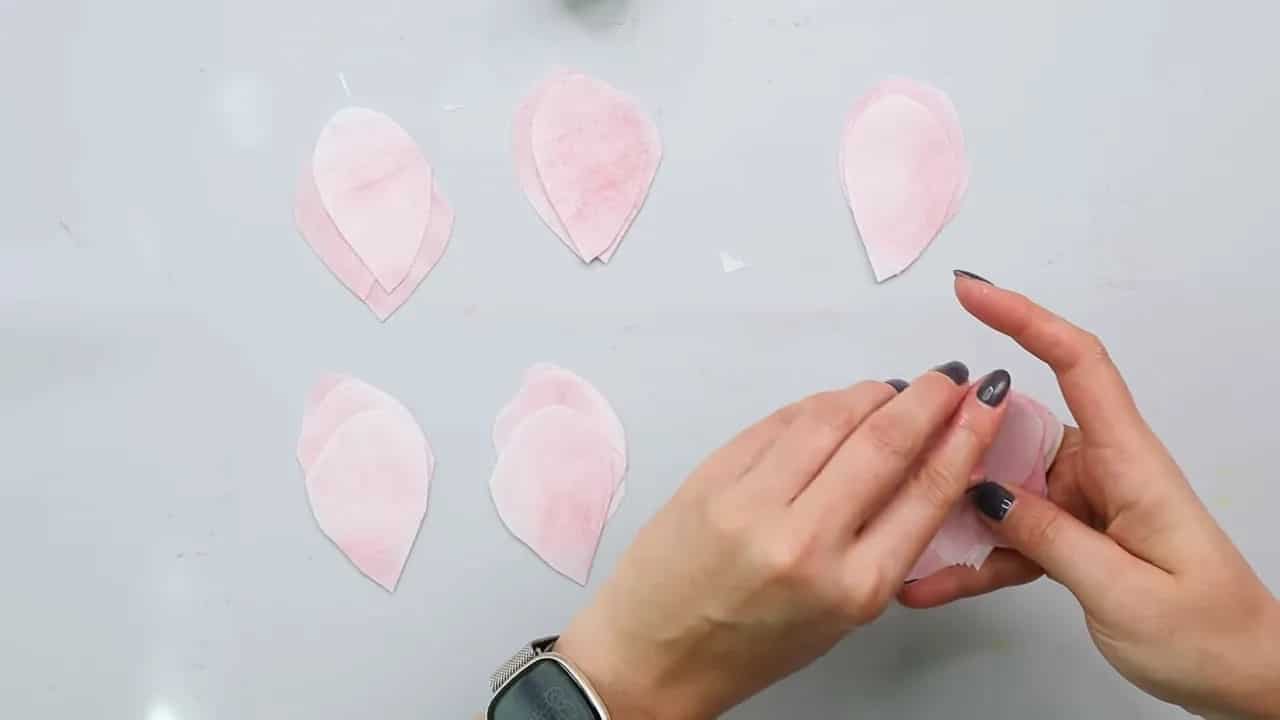 Hands adjusting multiple pink wafer paper petals on a work surface