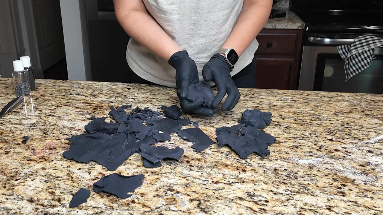 Assembling irregular black fondant pieces into a rough stone texture base for wedding cake decorating