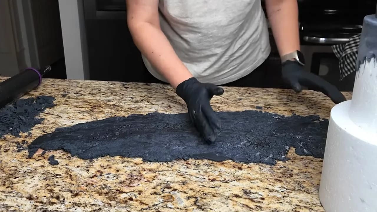Hands smoothing black textured fondant on a dummy wedding cake tier without overlap