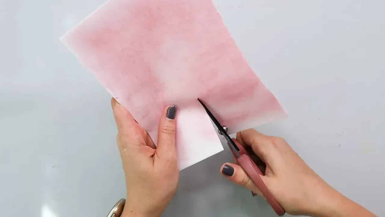 Scissor cutting pink wafer paper into petal shapes