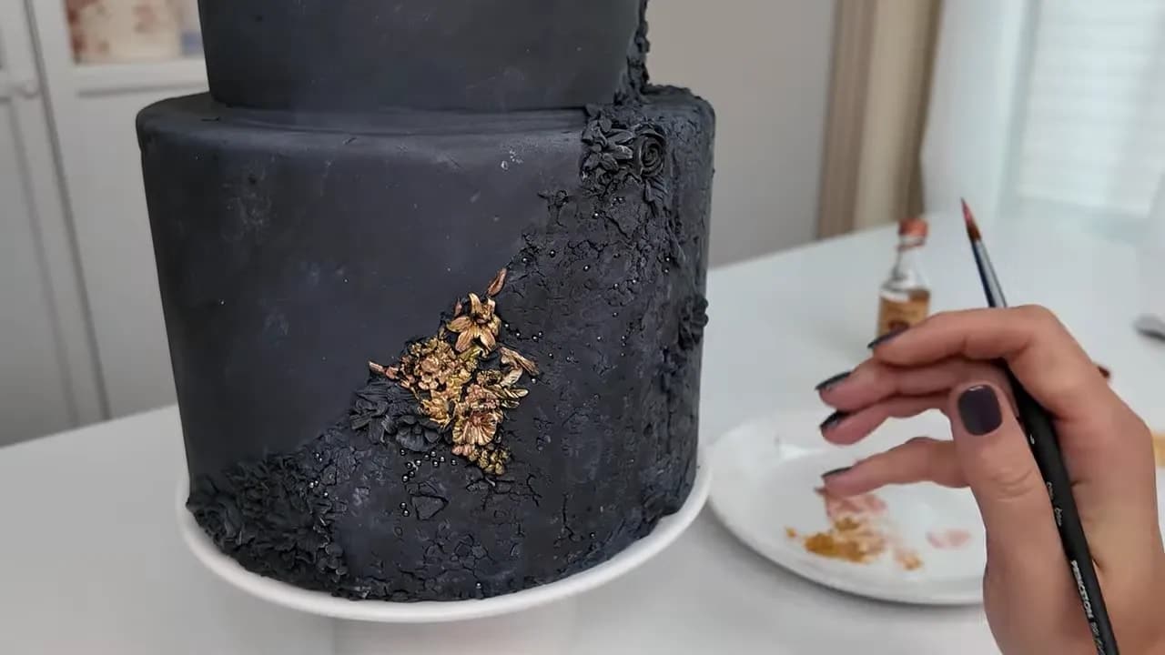 Dummy wedding cake being painted with gold accents over black fondant rough stone texture