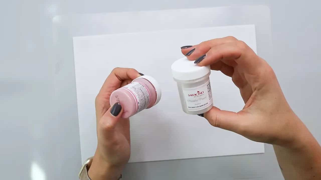 Hands holding pink and pearl coloring powder bottles next to wafer paper on a sheet for making wafer paper flowers