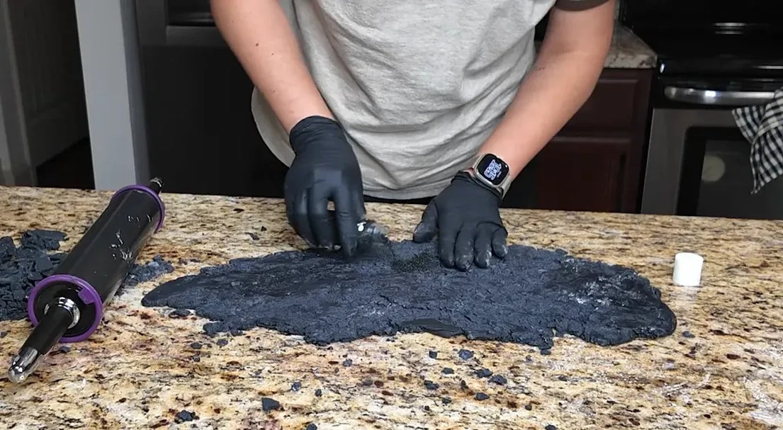 Hands pressing sanding sugar and nonpareils into a rough black fondant texture