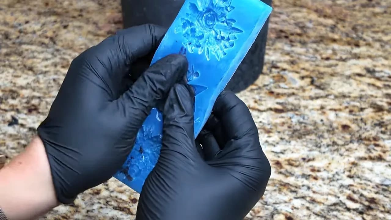 Gloved hands pressing thin black fondant into a silicone mold to create bas-relief detail