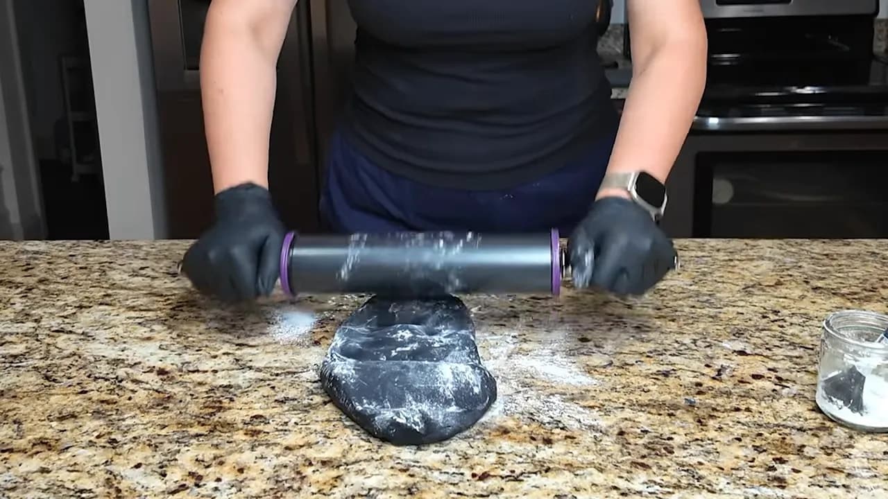 Baker rolling black Satin Ice fondant to an even thickness using a rolling pin with spacers