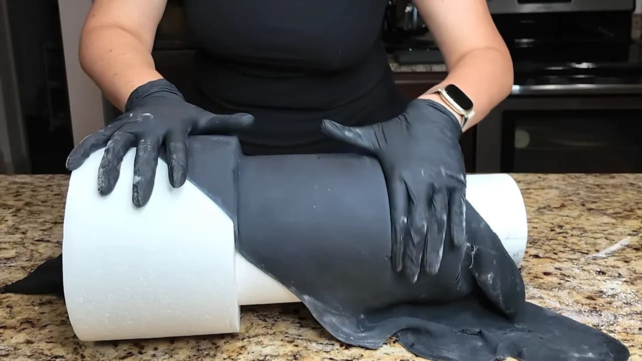 Hands smoothing black fondant over a dummy cake tier to create the base layer